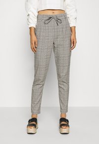 Grijze geruite broek met een tailleband met trekkoord, taps toelopende pijpen en zijzakken, gecombineerd met zwarte platform sandalen en een cropped witte top.