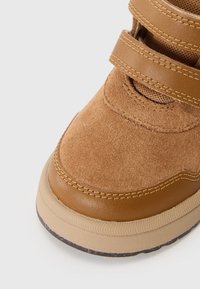 Bottines en daim et cuir tan avec deux sangles tan, bout rond et semelle en caoutchouc texturée. Détails cousus sur la tige.