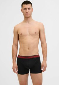 Schwarze Baumwollboxershorts mit einem roten Bund, auf dem der Markenname "JACK & JONES" prominent abgebildet ist. Elastisches Material und figurbetonte Form.
