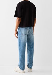 Czarny krótki t-shirt, jasnoniebieskie jeansy z przetarciami i tylnymi kieszeniami oraz beżowe sneakersy. Luźny, casualowy styl, krótki rękaw, swobodny wygląd.