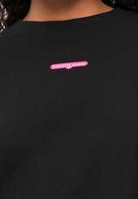 Hanorac negru cu guler rotund, realizat din bumbac, având un patch logo roz "tommy jeans" pe partea din față. Textură netedă, croială standard.