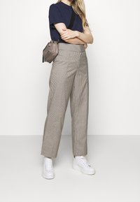Beige ternede højtaljede bukser med lige ben, parret med en navy t-shirt og hvide platform sneakers. Lille grå crossbody taske.