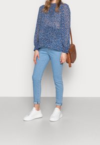 Blå blommig blus med lång ärm, lättviktsmaterial, dra ihop manschetter, matchad med ljusblå smaljeans och vita sneakers. Brun axelremsväska.