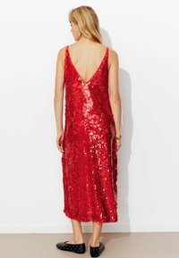 Robe rouge à sequins avec un dos en V, longueur mi-mollet et silhouette ajustée. Texture lisse avec des sequins brillants sur toute la surface.