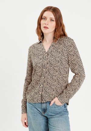 Chemise boutonnée à imprimé léopard beige et noir, avec col, manches longues et coupe décontractée, associée à un jean bleu clair.