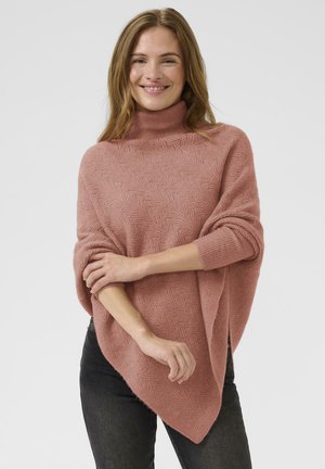 Pink knit poncho with a high neck, featuring a textured herringbone pattern and loose fit, draping elegantly over dark jeans.