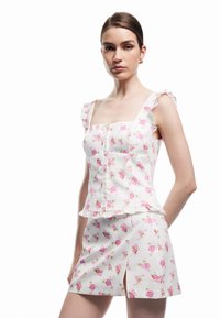 Top corto blanco de flores con rosas rosas, tirantes con volantes y detalles de botones, combinado con una falda mini a juego con una abertura lateral.