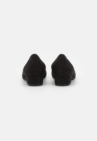 Chaussures à talons en suede noir avec un bout rond et un petit talon carré, présentant une texture lisse et un design minimaliste.