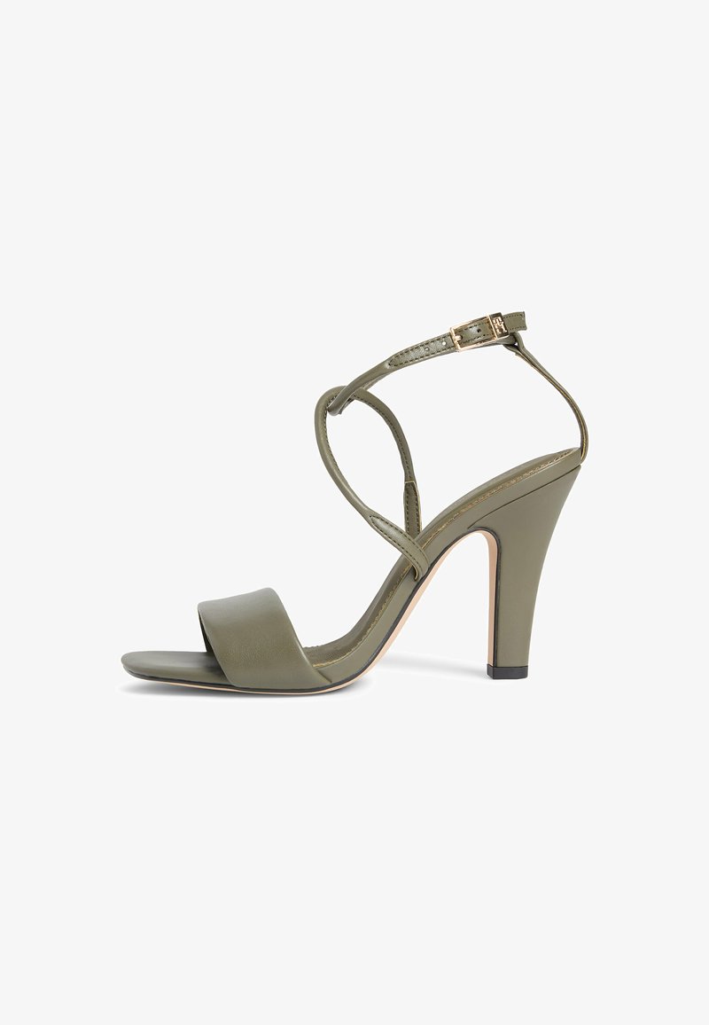 Sandale à talon haut vert olive à bout ouvert, avec une fine bride autour de la cheville ornée d'une boucle dorée, et un talon bloc, sur fond blanc.