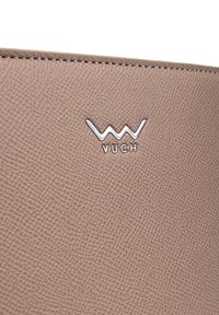 Texturovaný kožený povrch v taupe barvě se stříbrným logem značky VUCH a švy podél horního okraje materiálu.