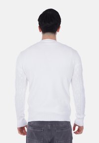 Maglione bianco lavorato a maglia con scollatura a costine e dettagli a treccia sulle maniche. Texture liscia e silhouette aderente.