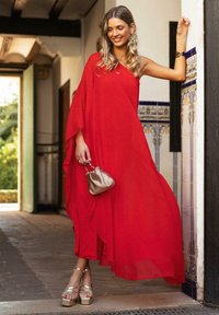Vestido rojo de un solo hombro, hecho de una tela ligera, de diseño fluido, combinado con tacones de plataforma dorados y un pequeño clutch metálico.
