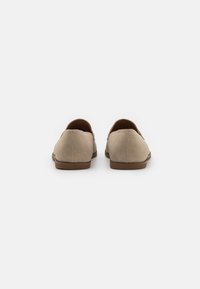 Chaussures en daim beige à enfiler avec un design profilé bas, semelle en caoutchouc beige et détails cousus à l'arrière. Esthétique propre et minimaliste.