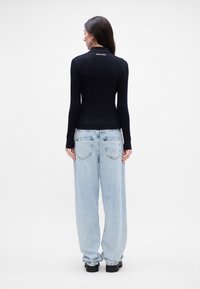 Čierny rebrovaný top s dlhými rukávmi a priliehavým strihom, kombinovaný s voľnými svetlomodrými džínami a čiernymi hrubými topánkami. Logo značky na krku.