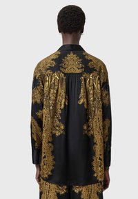 Black satin shirt with gold ornate pattern, long sleeves, and pleated back detailing. Features a classic collar and buttoned cuffs.