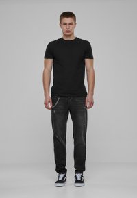 Camiseta negra, pantalones vaqueros negros desgastados con detalle de cadena en la cintura y zapatillas negras con acentos blancos. Diseño sencillo y ajustado.