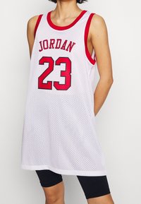 Vit baskettröja med röda detaljer, med "JORDAN" och "23" tryckt i röd och svart. Tillverkad i nättröja för god andningsförmåga.