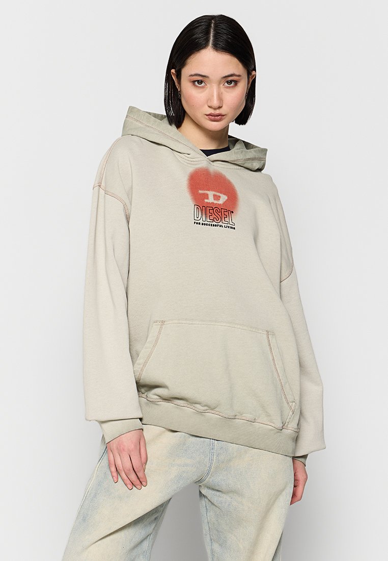 Sweat à capuche beige avec une grande poche avant, des poignets côtelés et une texture douce. Présente un graphique circulaire rouge avec le logo "DIESEL" sur la poitrine.