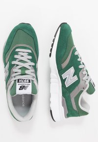 Zelené a šedé tenisky vyrobené z semiše a síťoviny, s tkaničkovým designem, gumovou podrážkou a výrazným logem 'N' na bocích.