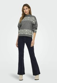 Pull gris en tricot avec des motifs géométriques, col montant et manches longues, associé à un pantalon évasé noir et des bottines beiges.