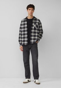 Geruit flanellen overhemd in zwart en wit, gecombineerd met een donkere henley. Slanke grijze jeans en witte sneakers met grijze en bruine accenten.