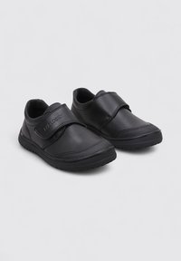 Zapatos de piel negra con correa de velcro, puntera redondeada, diseño texturizado y suela de goma. Adecuados para el uso casual con una apariencia minimalista.