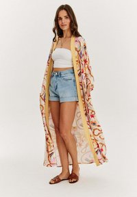 Dlouhý kimono s květinovými a abstraktními vzory v růžové, žluté a krémové barvě; lehká tkanina; otevřený přední díl; spárováno s denimovými šortkami a sandály.