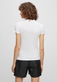 Biała koszulka polo z krótkim rękawem o gładkiej fakturze, z kołnierzykiem i dopasowanym krojem, w komplecie z czarnymi szortami o fakturze.