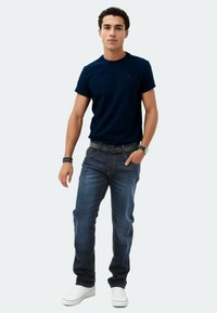Navy cotton t-shirt paired with blue jeans. The jeans feature a slim fit, and the outfit includes white sneakers and a black belt.
