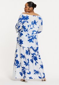 Witte off-the-shoulder blouse en bijpassende maxi rok met gedurfde blauwe bloempatronen, met een lichte textuur en een relaxte pasvorm.