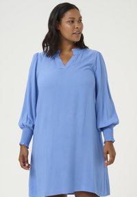 Lichtblauwe jurk van een textuurstof, met V-hals, lange pofmouwen en gerimpelde manchetten. A-lijn model, tot aan de knie.