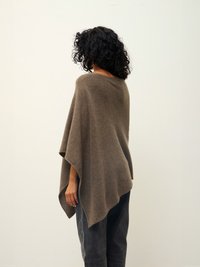 Hnědý vlněný pončo s volným, splývavým designem, s vysokým límcem a asymetrickým lemem, nošený přes tmavé, volně střižené kalhoty.
