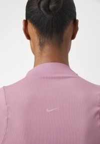 Rosa treningsgenser med krage, kort erm og en subtil Nike-logo på baksiden, laget av glatt stoff med teksturert overflate.