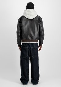 Läderbomberjacka i mörkbrunt med en grå huva, ribbade ärmslut och en avslappnad passform. Matchad med lösa mörka denimjeans med stora fickor.