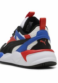 Baskets Puma avec une tige en mesh noire, blanche et bleue, rehaussée d'accents rouges. Détails texturés remarquables et semelle blanche rembourrée.