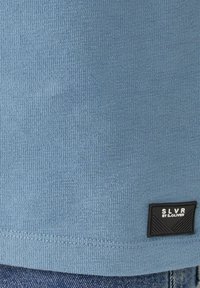 Lichtblauwe gestructureerde stoffen T-shirt met ribbelontwerp, voorzien van een zwart merklabel op de onderste linkerrand.