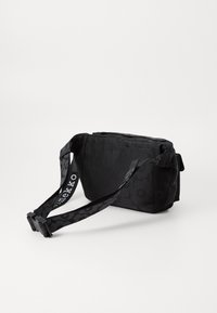 Sac bandoulière en tissu noir avec un motif floral texturé, une bandoulière réglable et un fermoir à boucle. Forme rectangulaire compacte.