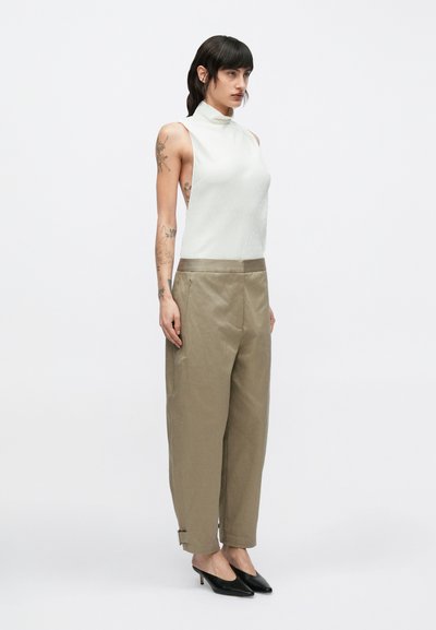 Biely tielkový top s vysokým golierom, v kombinácii s voľnými béžovými nohavicami so zipsom na boku a ohrnutým lemom, nosené s čiernymi lodičkami.