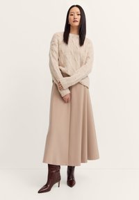 Hellbeige, grob gestrickter Pullover, langer beiger Rock und dunkelbraune spitze Knöchelstiefel mit Krokodilprägung. Schlichtes, warmes Design.