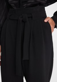Czarne spodnie z wysokim stanem z szerokim paskiem, z plisowanym przodem i bocznymi kieszeniami. Wykonane z gładkiego, teksturowanego materiału.