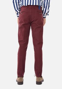 Pantaloni bordeaux in cotone con taglio dritto, tasche posteriori con chiusura a bottone e orlo maniche, abbinati a scarpe marroni.