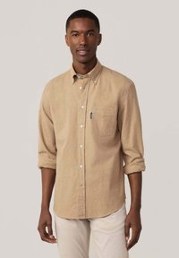 Camisa de botones de color marrón claro con un bolsillo, mangas arremangadas y una textura suave. Tiene botones blancos y un sutil patrón jaspeado.