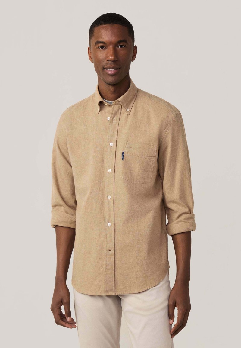 Camisa de botones de color marrón claro con un bolsillo, mangas arremangadas y una textura suave. Tiene botones blancos y un sutil patrón jaspeado.