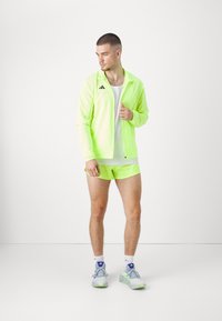 Neoonkollane spordijope ja lühikesed püksid, valge alussärk. Tennised on helesinised roheliste aktsentidega. Omab minimalistlikku disaini ja brändingut.