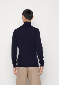 Marint blå polotröja, tillverkad av mjukt tyg, med långa ärmar och en figurnära design, med ribbade mudd och nederkant.