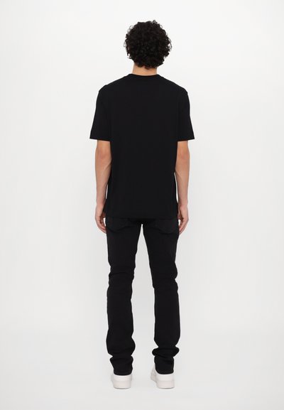 Juoda medvilninė T-marškiniai su trumpomis rankovėmis, tiesaus kirpimo ir apvalia iškirpte, derinama su juodomis džinsomis ir baltomis sportbačiais. Paprasta dizaino, be raštų.