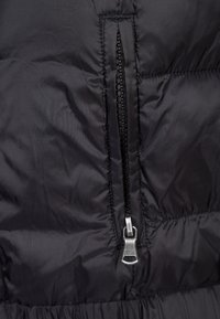 Section de veste matelassée noire avec fermeture éclair à tirette argentée, tissu texturé et détails cousus.