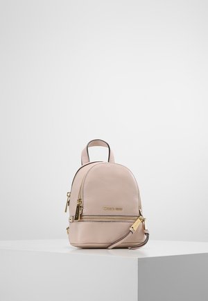 Lille beige læderrygsæk fra Michael Kors med gyldne lynlåse og logo, med topgreb og forreste lynlåslomme, vist på en hvid piedestal.