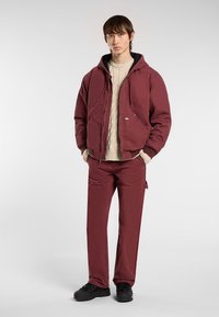 Bordeaux zip-up bomberjakke med hætte og forlommer, parret med matchende bordeaux bukser og sort fodtøj. Chunky creme sweater under.