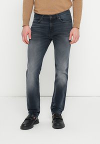 Blugi din denim albastru închis, croială slim, cu cinci buzunare, ușor decolorați și cu fermoar și nasture la brâu. Asortați cu pantofi negri.